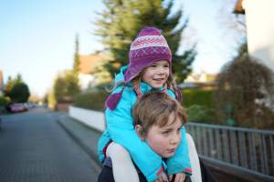 little sister riding on her borthers shoulders happy dressed warm